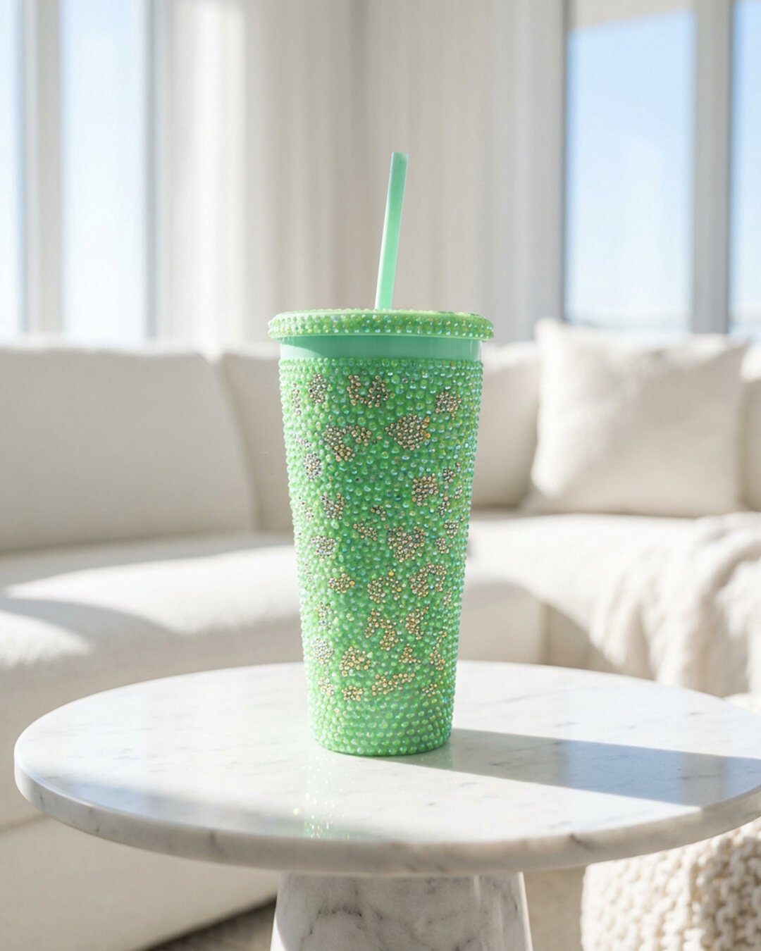 Mint green tumbler fully covered in green and iridescent crystal, on a marble table